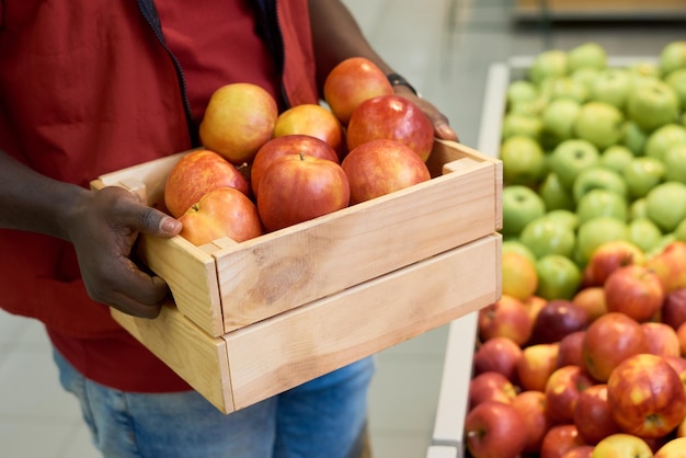 Mãos de jovem negro segurando uma caixa de madeira com maçãs vermelhas maduras frescas