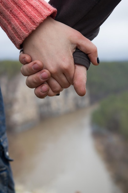 Foto mãos de jovens caminhantes em pé na beira de um penhasco sobre o rio da montanha fecham