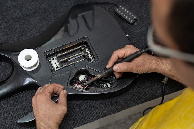 Mãos de Luthier soldando fios de microfone de guitarra elétrica com ferro de solda e estanho