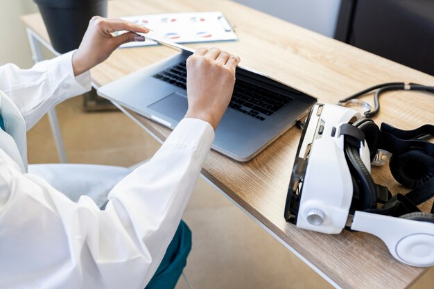 Mãos de médica com laptop e óculos de realidade virtual