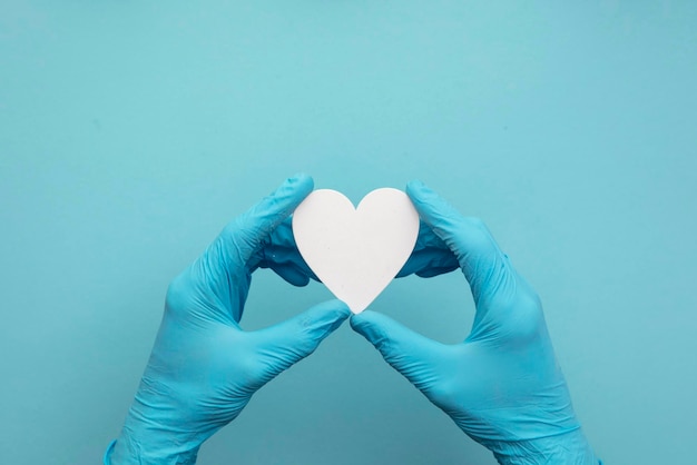 Mãos de médicos usando luvas cirúrgicas azuis segurando uma forma de coração branco