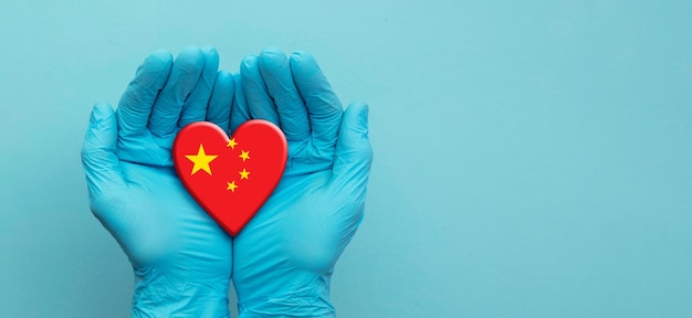 Mãos de médicos usando luvas cirúrgicas segurando o coração da bandeira da china