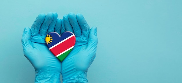 Mãos de médicos usando luvas cirúrgicas segurando o coração da bandeira da namíbia