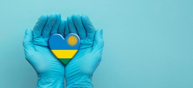 Mãos de médicos usando luvas cirúrgicas segurando o coração da bandeira de Ruanda