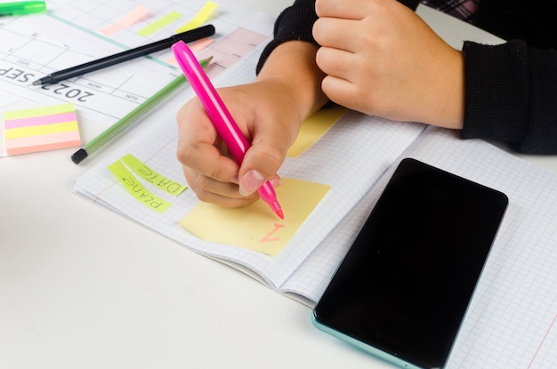 Mãos de menina com celular com calendário escrito e lista de trabalho no diário na mesa