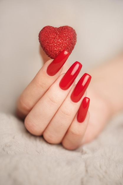 Mãos de menina com manicure vermelha e coração decoratine