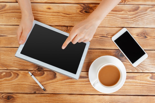 Mãos de menina com tablet digital e xícara de café em uma mesa de madeira