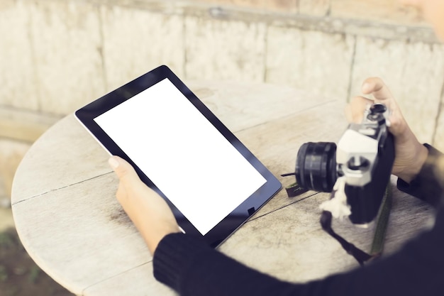 Mãos de menina com tablet digital em branco e câmera velha em uma mesa de madeira