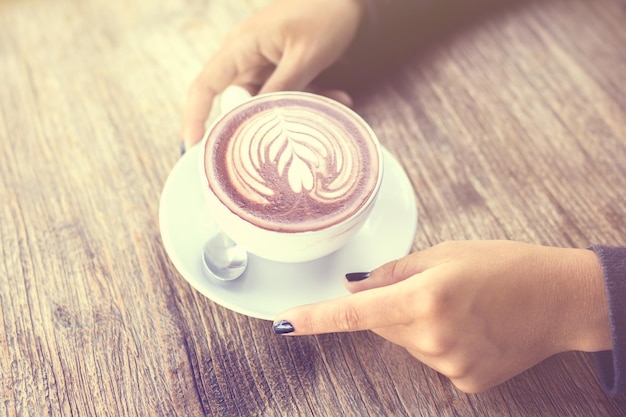 Mãos de menina com xícara de cappuccino em um efeito de foto vintage de mesa de madeira