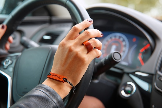 Mãos de menina no volante de um carro, uma pulseira com a inscrição do sonho nas mãos