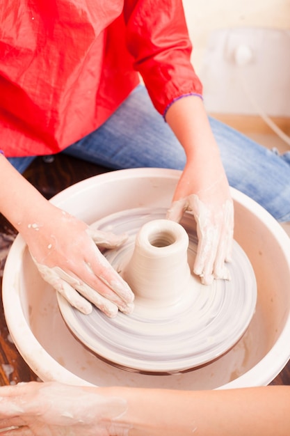 Mãos de menina que faz cerâmica de argila branca em uma roda de oleiro