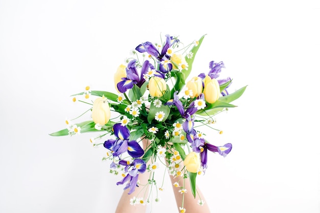 Mãos de menina segurando um lindo buquê de flores: tulipas, camomilas, flor de íris em fundo branco. camada plana, vista superior. composição floral