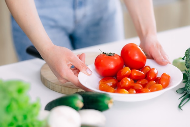 Mãos de menina segurando um prato de tomate, coloca na mesa, para preparar salada.