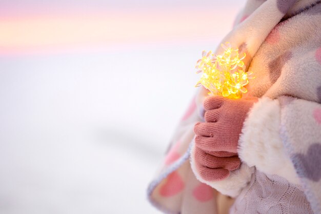 Mãos de menina segurando uma sequência de luzes de bokeh.