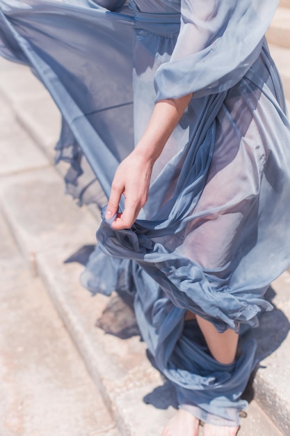 Mãos de meninas com os pés em um vestido azul wusasa pela brisa do mar de verão