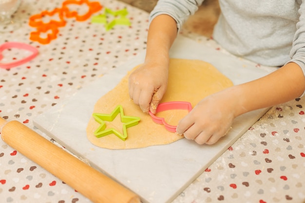 Mãos de menino pré-escolar fazendo biscoitos usando moldes de biscoito