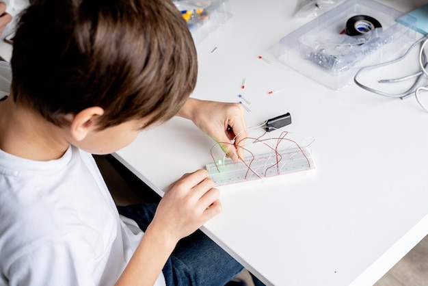 Mãos de menino trabalhando com luzes led em uma placa experimental para projeto de ciências