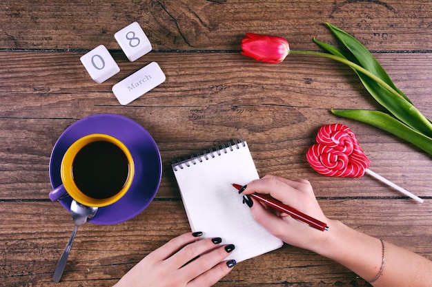 Mãos de Moman escrevendo saudações flor de tulipa rosa pirulito o calendário de bloco de data
