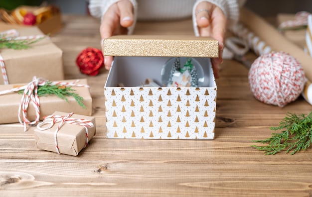 Mãos de mulher abrem presente de Natal com bola de neve fecham presentes não preparados no fundo de madeira