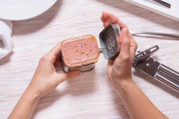 Mãos de mulher, abrir a lata com carne em lata, mesa da cozinha vista superior