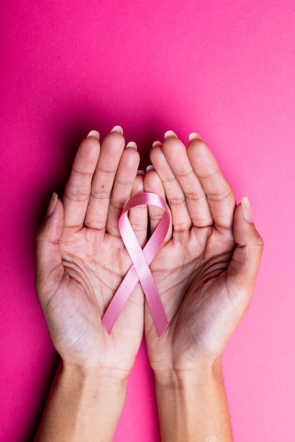 Foto mãos de mulher adulta média afro-americana segurando fita rosa de conscientização sobre o câncer de mama, espaço de cópia. fundo rosa, mama, câncer, conceito médico, de conscientização, de apoio, de saúde e de alerta.