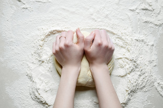 Foto mãos de mulher amassa a massa com farinha na mesa da cozinha branca. vista superior plana leigos.