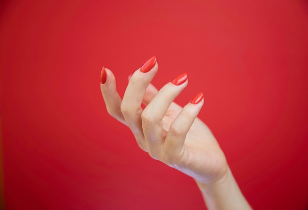 Mãos de mulher bem cuidada sobre fundo vermelho.