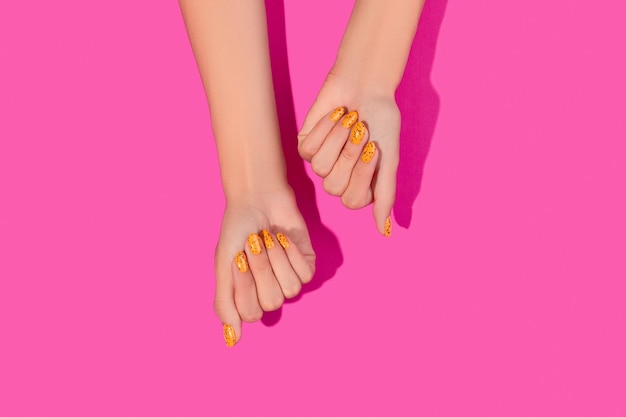 Mãos de mulher bem cuidadas com design de unhas na moda em fundo rosa