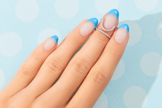 Mãos de mulher bonita com design de unhas na moda no fundo azul