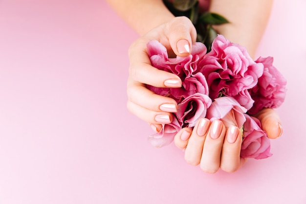 Mãos de mulher bonita com eustoma fresco. Conceito de spa e manicure. Mãos femininas com manicure rosa. Conceito de pele suave. Unhas de beleza. Sobre fundo bege