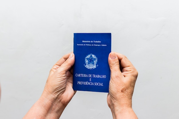 Foto mãos de mulher caucasiana sênior segurando carteira de trabalho, documento da previdência social brasileira