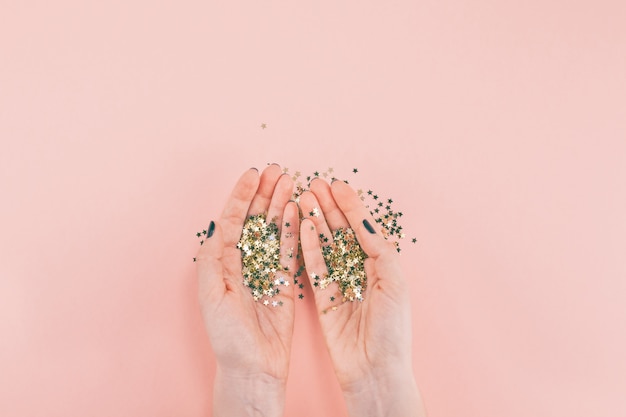 Mãos de mulher cobertas de confetes de estrelas douradas em rosa