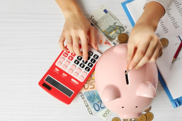 Mãos de mulher colocando moedas de euro em um cofrinho e contando com a calculadora na mesa Conceito de economia financeira