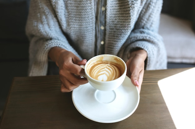 Mãos de mulher com cappuccino na mesa de madeira