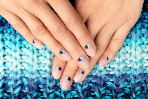 Mãos de mulher com desenho de unhas nude e azul fosco em suéter de malha de lã