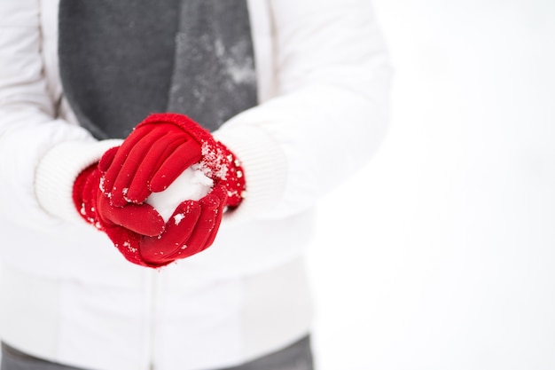 Mãos de mulher com luvas vermelhas fazendo uma bola de neve