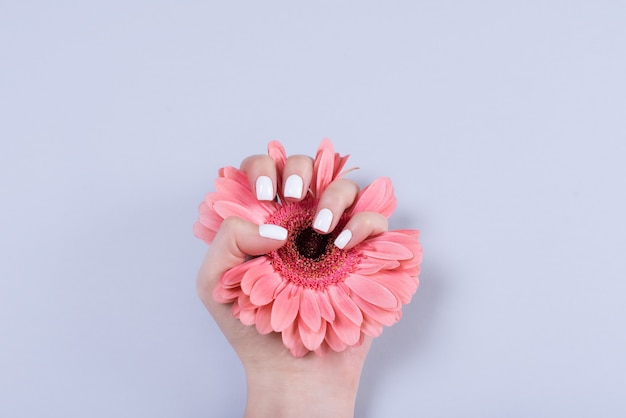 Mãos de mulher com manicure e aliança entre renda branca e pequenas flores