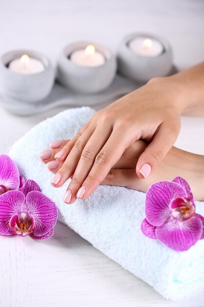 Foto mãos de mulher com manicure francesa e flores de orquídea na mesa de madeira fechada