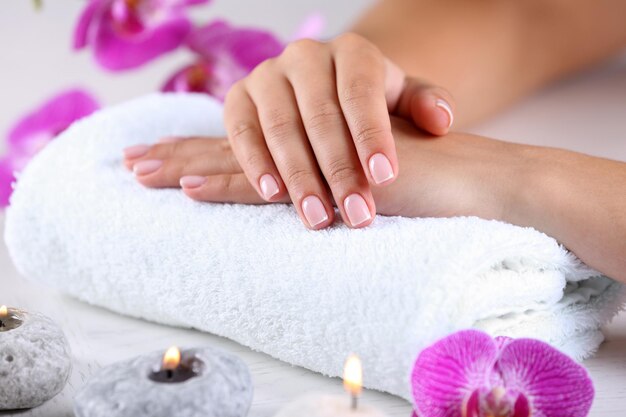 Mãos de mulher com manicure francesa e flores de orquídea na mesa de madeira fechada