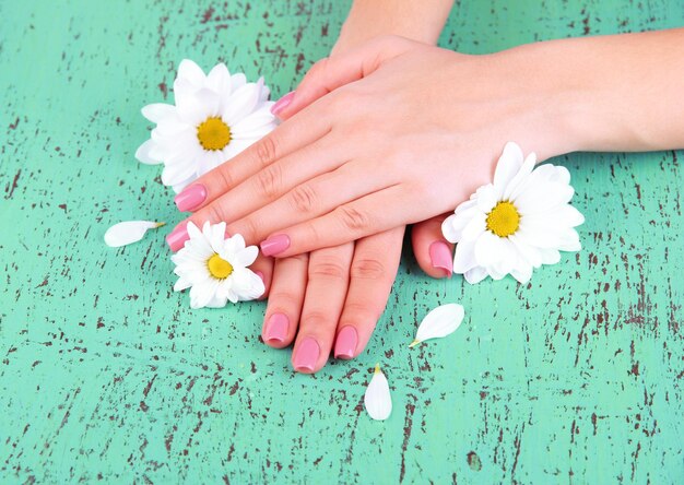 Mãos de mulher com manicure rosa e flores na cor de fundo