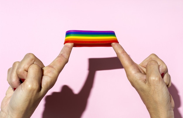 Mãos de mulher com pulseira lgbt em fundo rosa