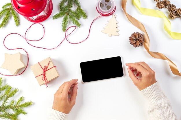 Mãos de mulher com telefone celular, presentes de Natal e decorações em fundo branco