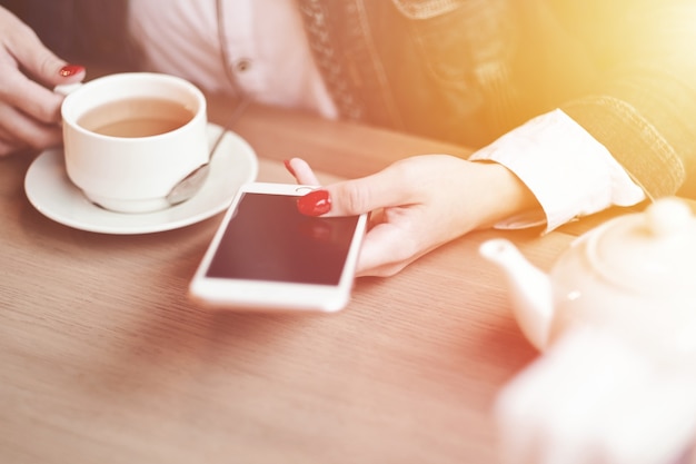 Mãos de mulher com telefone inteligente, fones de ouvido e uma xícara de chá. Para montagem de display gráfico