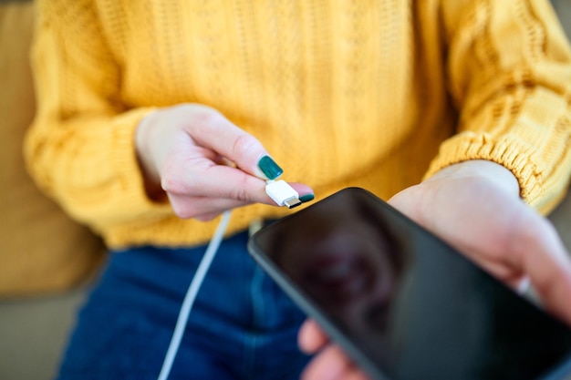 Mãos de mulher conectando um carregador em um smartphone Mulher usando smartphone com powerbank carregando energia para smartphone Mulher carregando bateria no celular em casa