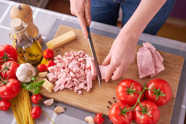 Mãos de mulher cortando bacon de presunto pancetta na tábua de madeira na cozinha doméstica