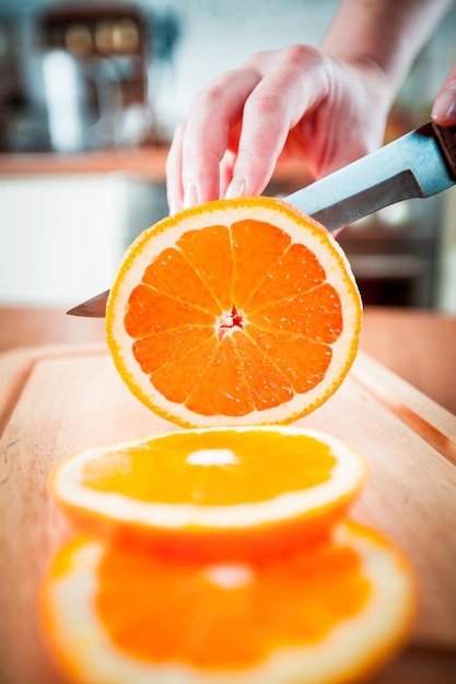 Foto mãos de mulher cortando laranja fresca na cozinha