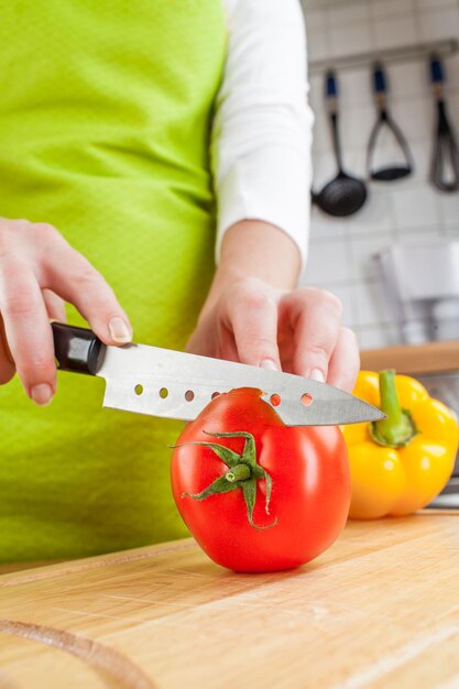 Mãos de mulher cortando tomate fresco na cozinha