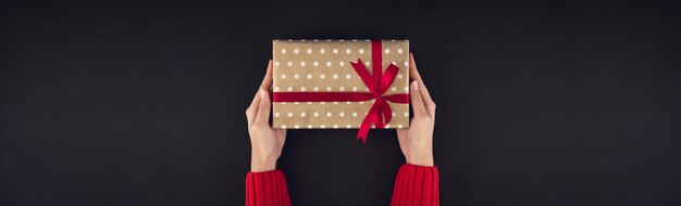 Mãos de mulher dando caixa de presente de Natal em fundo preto