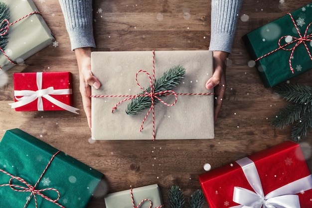 Mãos de mulher dando caixa de presente de Natal na mesa de madeira