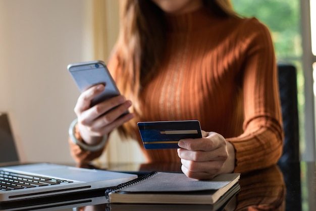 Mãos de mulher de negócios usando smartphone e segurando o cartão de crédito sentado. Conceito de pagamentos de compras online.